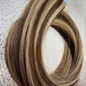 Tape-in hair extensions with natural blend of blonde and brown tones, showcasing smooth, straight remy human hair.