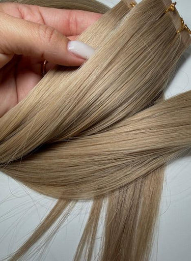Blonde human hair extensions with gold clips, held in hand for close-up view